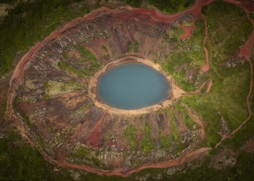 Aerial view of the Kerid Crater Lake's turquoise waters nestled within the stark red volcanic slopes contrasted against the vibrant green moss, Flugir, Rangarthing ytra, Iceland.