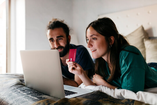 Happy couple lying on bed shopping online