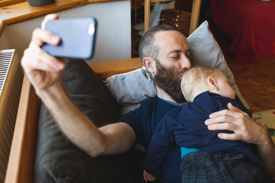 Man taking a selfie with his cute sleeping son on the sofa