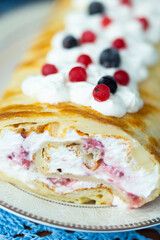 Homemade pancake roll called Finnish pancake with cream cheese and berry confit on table with blue lace tablecloth