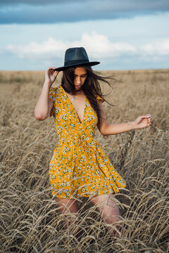 Young woman wearing summer dress with floral design and a hat dancing in corn field
