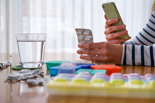 Close-up of woman taking medicine and using smartphone at home