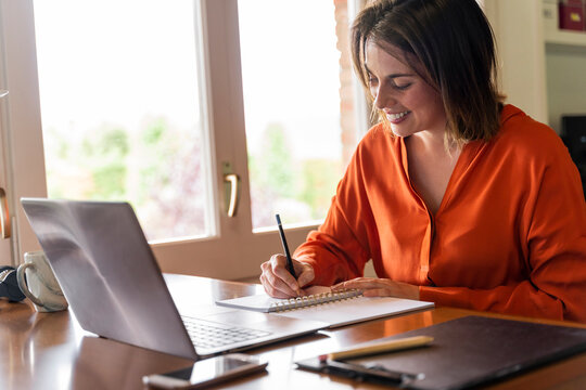 Smiling businesswoman writing in notepad while working at home