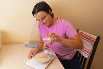 Female caucasian adult preparing dough in kitchen with phone recipe