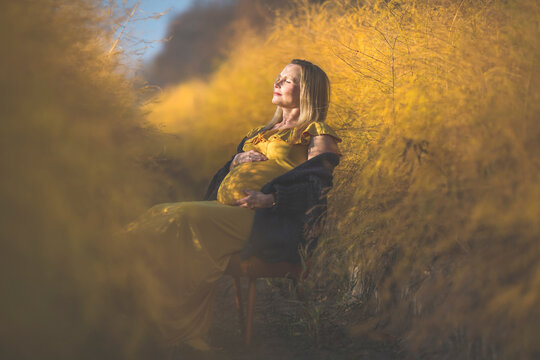 Pregnant woman sitting on chair in asparagus field in autumn