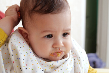 Portrait of little baby boy eating food. Baby with a spoon in feeding chair. Cute baby eating first meal