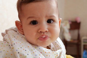 Portrait of little baby boy eating food. Baby with a spoon in feeding chair. Cute baby eating first meal