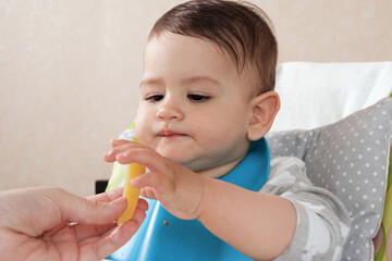 Portrait of little baby boy eating food. Baby with a spoon in feeding chair. Cute baby eating first meal