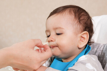 Portrait of little baby boy eating food. Baby with a spoon in feeding chair. Cute baby eating first meal