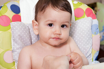 Portrait of little baby boy eating food. Baby with a spoon in feeding chair. Cute baby eating first meal