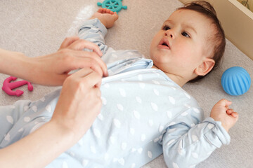 A mother dressing her little baby boy boy at home. childhood parenthood and growing up family concept real people