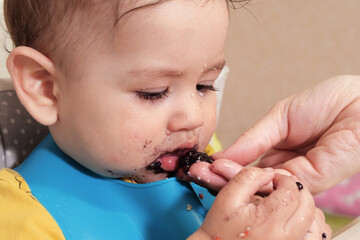 Portrait of little baby boy eating food. Baby with a spoon in feeding chair. Cute baby eating first meal