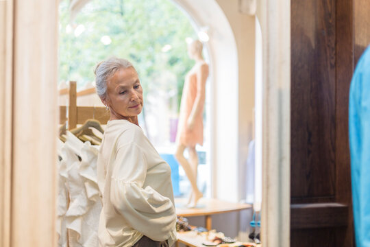 Smiling senior woman trying on pullover in a boutique