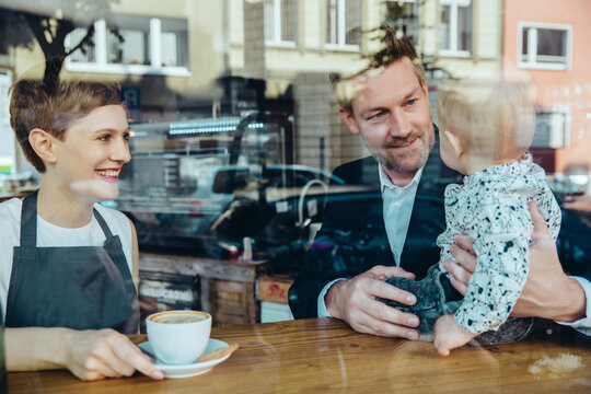 Waitress serving coffee to smiling customer with baby in cafe