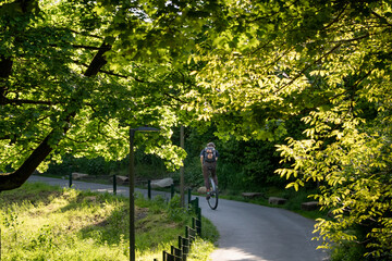 Fototapeta premium Person riding a unicycle on a quiet park pathway under fresh green trees. Clean transport concept, sustainable travel, individuality, outdoor activity, summer scene.