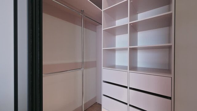A sleek modern wardrobe with sliding glass doors, open shelves, closed drawers, minimalist design, neutral tones, complemented by a wall lamp and decorative vase.
