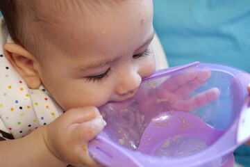 Portrait of little baby boy eating food. Baby with a spoon in feeding chair. Cute baby eating first meal