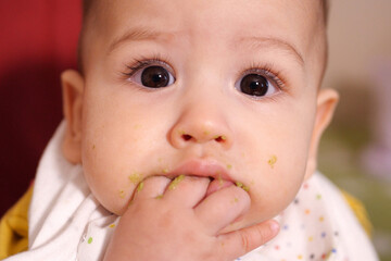 Portrait of little baby boy eating food. Baby with a spoon in feeding chair. Cute baby eating first meal