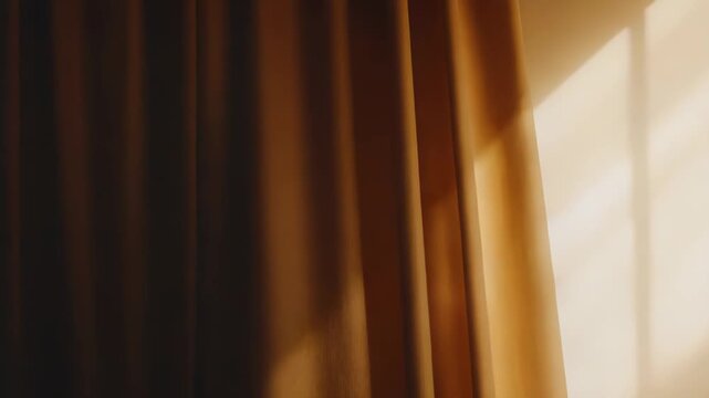 Golden brown fabric curtain hanging by a wall, illuminated by natural sunlight streaming through a window, casting abstract patterns and linear shadows on the floor and empty wall surface