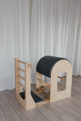Wooden Pilates ladder barrel machine positioned in minimalist home studio. Focus on natural materials, craftsmanship, and functional design highlights Pilates equipment in clean controlled setting © Anton