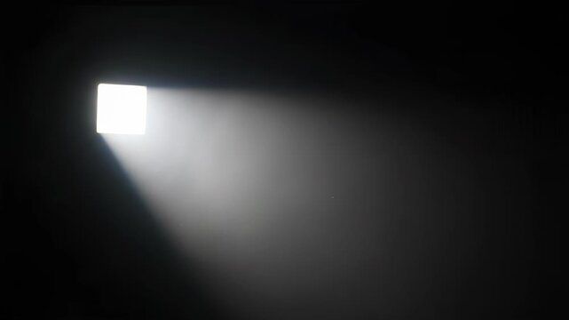 A beam of light shining through a small square opening in a dark room