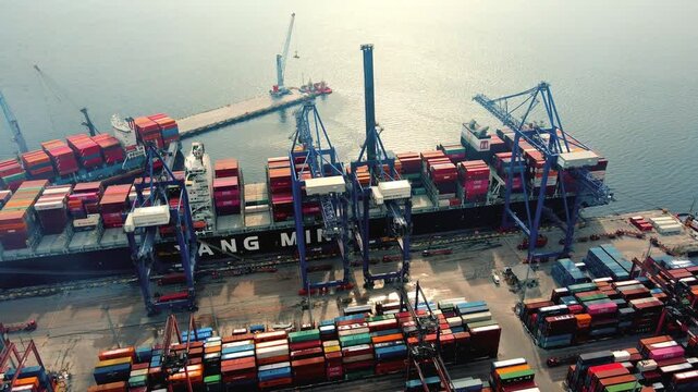 Aerial drone shot of a busy container port terminal with stacked cargo containers, cranes and ships. Industrial logistics, global trade, shipping and transportation infrastructure concept.