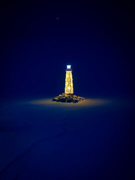 A lighthouse on a frozen shore on a night under Jupiter planet in the sky.