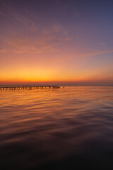 Fototapeta premium Serene Golden Sunset over Calm Sea with Wooden Pier Silhouette,A breathtaking long exposure shot of a vibrant sunset over the ocean, featuring a tranquil wooden pier stretching into the calm water. 