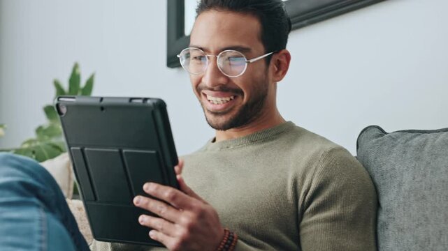 Man with a digital tablet watching funny video or movie on a sofa at home. Happy guy smile and laugh scrolling on social media and streaming movies online to enjoy over the weekend on the couch