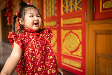 Happy Little Asian Girl in Red Traditional Cheongsam Celebrating Lunar New Year,A cheerful young East Asian girl wearing a traditional red and gold floral qipao (cheongsam) stands smiling in front.