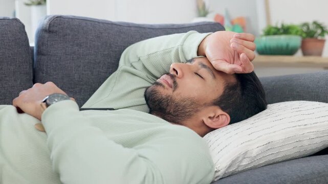 Upset, frustrated and sad young male lying, thinking and contemplating on a living room couch. Depressed man lounge on a sofa feeling unhappy, guilty and struggling with mental health indoors