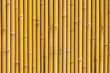 A textured wall made of vertically arranged bamboo stalks, showcasing their natural yellow color and rhythmic patterns.