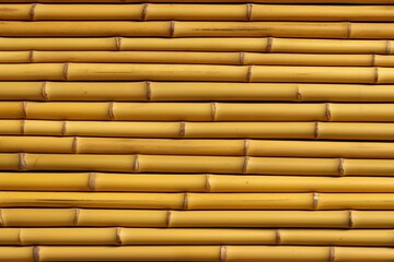 A close-up of yellow bamboo sticks arranged neatly, showcasing their natural texture and color in a horizontal layout.