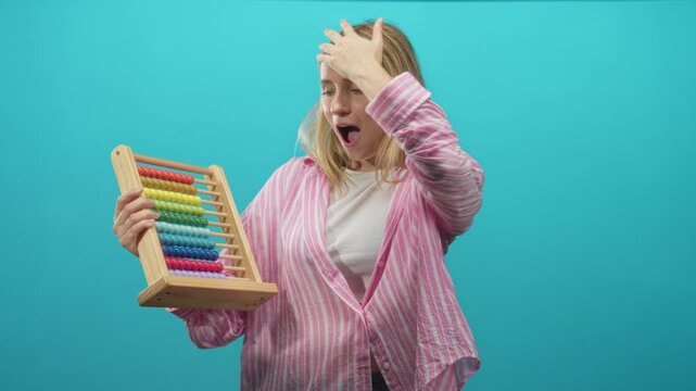 Woman holding abacus, hand on forehead and mouth open in studio with turquoise backdrop; surprise realization.
