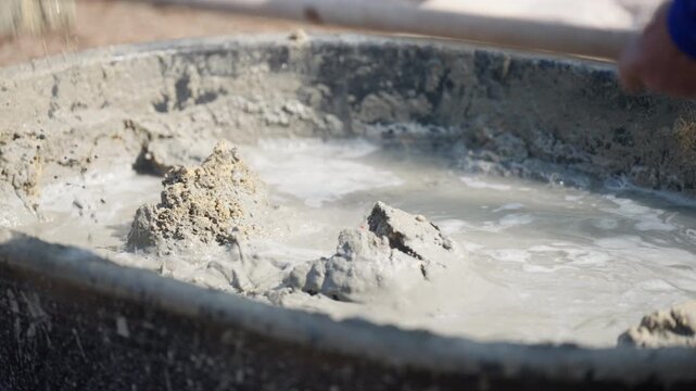 Wet cement mixture with sand and water in plastic tub at outdoor construction site, showing raw building material preparation.
