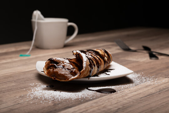 crepe o panqueque relleno con manjar, espolvoreado  con az&uacute;car flor y ba&ntilde;ado en salsa de chocolate