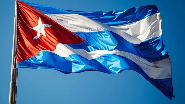 Cuban flag waving in the wind under a clear blue sky, displaying its iconic design of red triangle, white star, and alternating blue and white stripes, representing the nation's pride and heritage