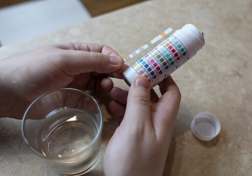 A man in the kitchen tests tap water quality with a test strip. Home testing for drinking water safety, pH, chlorine, and chemical contaminants.