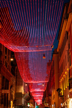 City street decorated with red LED light installation at night. Modern urban scene with strong perspective, vibrant illumination and festive atmosphere.