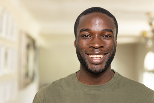 African American man smiling at camera, wearing olive crewneck in softly lit home with framed art