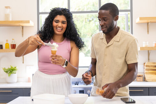 Diverse couple woman in pink top man in beige shirt scooping waffle cones in home kitchen