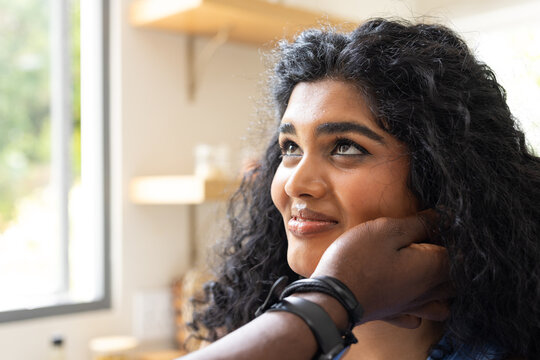 Female in top gazing toward large window as dark-skinned hand cupping cheek showing black watch