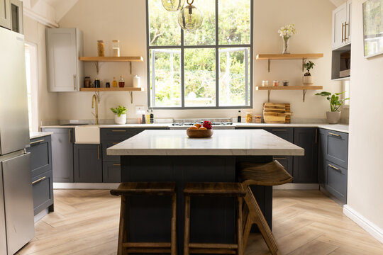 Central kitchen island is sitting on herringbone wood floor in bright kitchen, with bowl of fruit