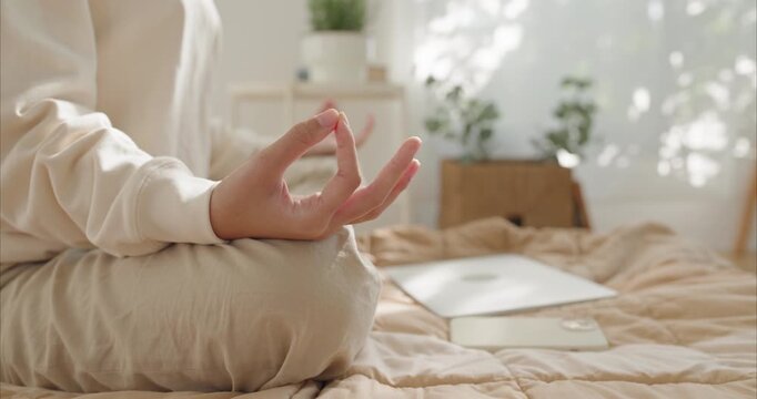 Close up of teenage female hands in mudra pose meditating on bed, digital detox concept with smartphone and laptop ignored in background, mindfulness and mental health in warm morning sunlight.