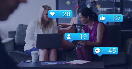 Reviewing laptop, tablet, two women in office lounge in white blazer and magenta top, social icons