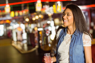 Woman standing right side at arcade wearing denim lace top holding glass pink drink, copy space