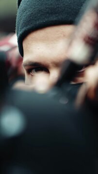 Close up of a sniper observing through weapon optics during mass protests, concept of surveillance, fear and suppression of demonstrations in authoritarian regimes