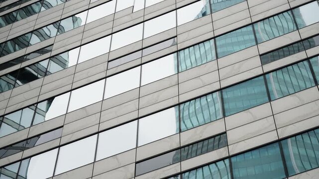 Diagonal glass facade with reflective windows capturing a curving skyscraper, showcasing contemporary urban architecture, geometric patterns, and sleek metal cladding in daylight
