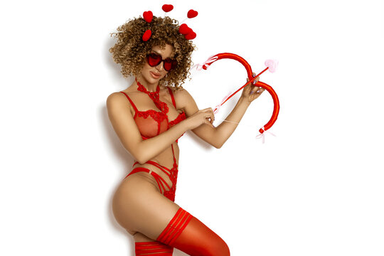 sexy young woman as cupid in red lace lingerie wings and stockings holding bow and arrow for valentine's day celebration isolated on white background