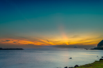 Obraz premium Witness the serene sunrise at Keelung Islet, Waishuangxi, Taiwan. Enjoy vibrant orange and blue skies with fast-moving clouds during a stunning summer morning.